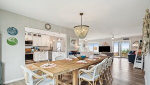 A spacious kitchen with white cabinets, a wooden dining table, wicker chairs, and a chandelier. - Oceanfront Luxury Home with Large Deck & Direct Beach Access - No Egrets (Folly Beach)