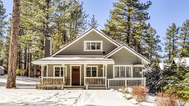 Une maison à deux étages avec un porche à l’avant, une cheminée et une allée recouverte de neige.