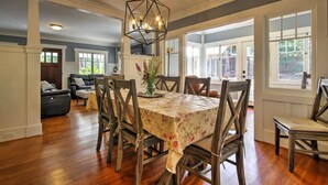 Un espace repas avec une table et des chaises en bois, un lustre aux motifs géométriques et de grandes fenêtres.