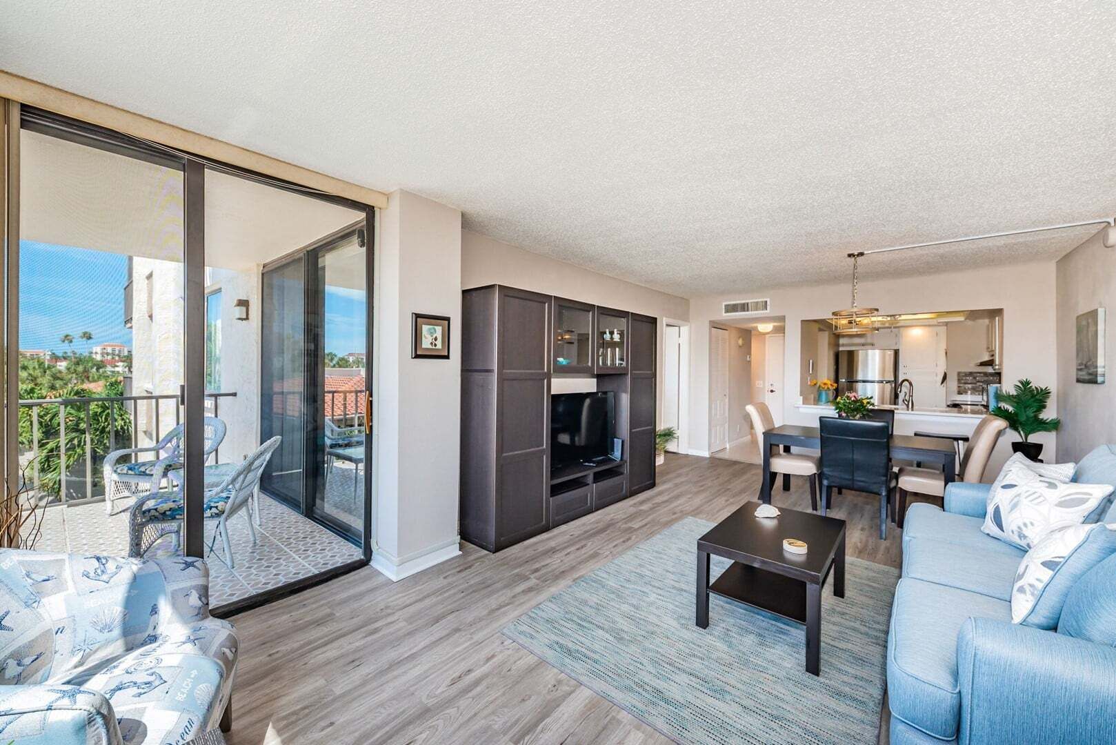 A modern apartment with a living room, dining area, and kitchen. There is a balcony with outdoor furniture.