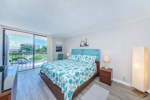 Een slaapkamer met een bed, nachtkastje, lamp, raam en uitzicht op de omgeving.