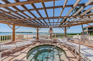 Een overdekt terras met een hottub, lounge stoelen, een zwembad en uitzicht op zee.