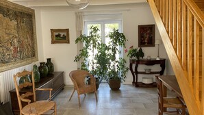 A spacious room with a wooden staircase, a large window with curtains, a dining table, and several wicker chairs. - Maison Individuelle, Preau Vers Piscine Privée Avec Plancha (Saint-Georges-du-Bois)