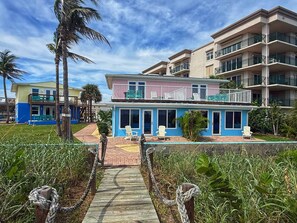 A multi-story hotel with balconies, a pool area, and a pathway leading to the entrance.