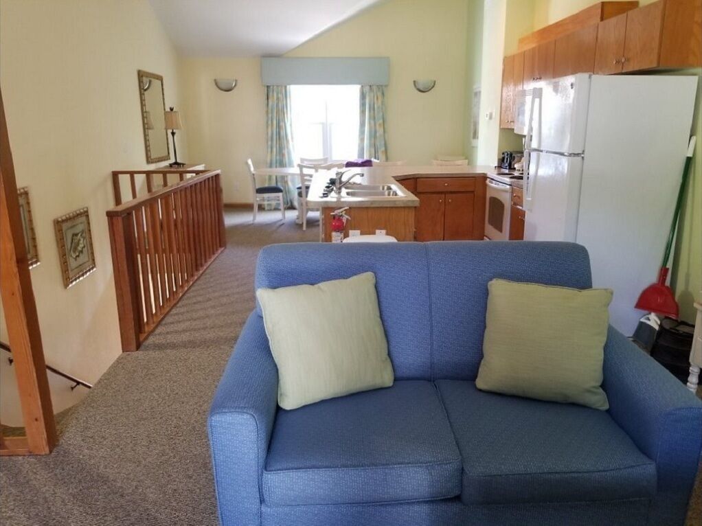 A living room with a blue sofa, a kitchen area with wooden cabinets, and a dining table with chairs.