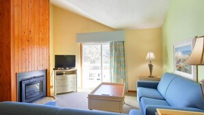 A living room with a fireplace, a television, a sofa, a coffee table, and a window with curtains. - Ocean Pines - 2BR/2BA Condo in Duck, NC (Duck)