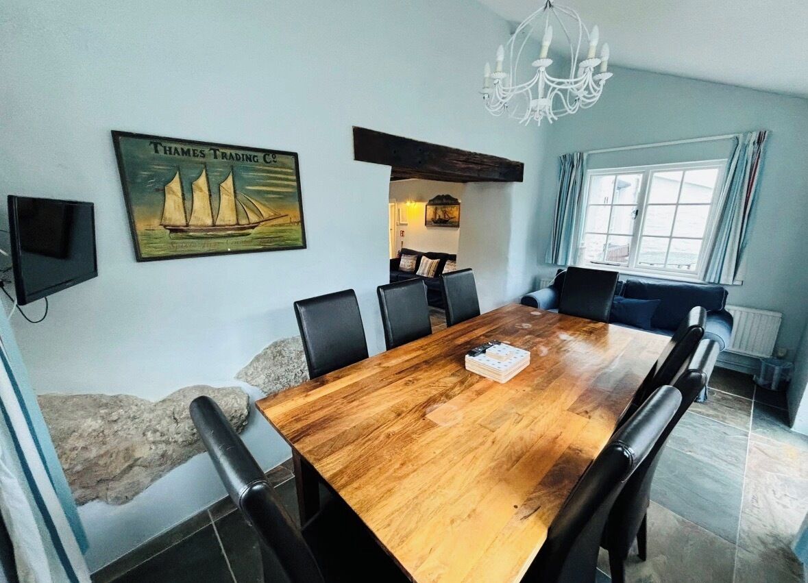 Ein Esszimmer mit Holztisch, schwarzen Stühlen, einer Chandelieber, einem Gemälde von einem Segelboot und Meerblick durch ein Fenster.