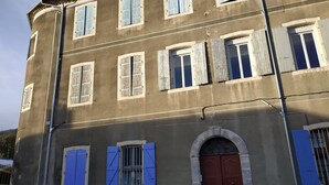 A multi-story building with a brown facade, multiple windows with shutters, and a central red door. - Location Montagne (Veynes)