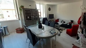 A dining area with a round table, chairs, and a cabinet. There is a sofa and a coat rack in the background. - Location Montagne (Veynes)