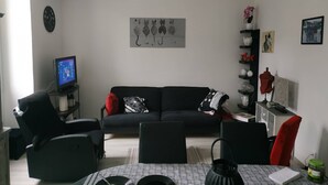 A living room with a black sofa, a TV, a coffee table, and a bookshelf with decorative items. - Location Montagne (Veynes)