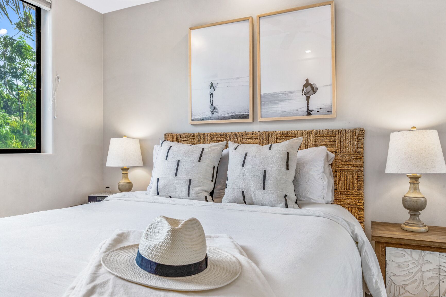 Quarto com cama grande, duas luminárias de cabeceira, cabeceira de fibra natural e duas imagens emolduradas na parede.