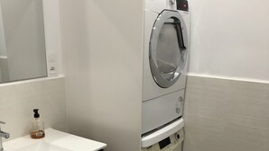 A modern bathroom with a white sink, wooden vanity, and a front-loading washing machine.