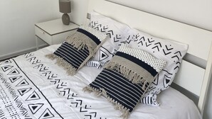 A neatly made bed with patterned bedding, a bedside table with a lamp, and a round mirror on the wall.