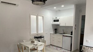 A compact kitchen with white cabinets, a microwave, and a sink. There is a dining table with chairs and a rug.
