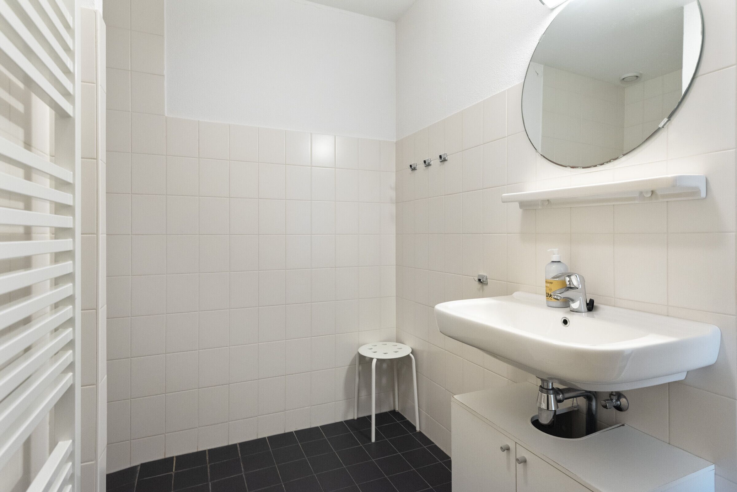 A bathroom with a white sink, a mirror, and a small stool.