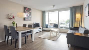 A modern living room with a dining table, grey sofa, and a large window offering a view of the city.