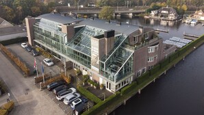 A modern hotel with a glass facade, a parking lot, and a river view.