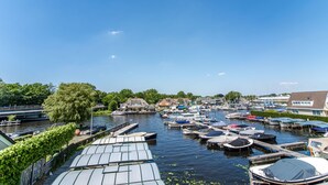 A marina with boats docked, a bridge in the background, and houses along the riverbank.