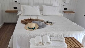 A neatly made bed with white linens, a wooden bench, and a straw hat on the bed. - Villa Campo das Medas, in the middle of nature, with private salt pool (Donas Gondomar)