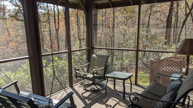 A covered outdoor seating area with a swing chair, two rocking chairs, and a small table.