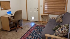 A room with a desk, chair, laptop, and a couch with a patterned throw pillow.