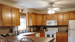 A kitchen with wooden cabinets, a central island with stools, a microwave, stove, and refrigerator.