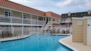 A swimming pool with lounge chairs and a building with balconies in the background. - North Wildwood Beach Block 1 bdrm with Pool. (North Wildwood)