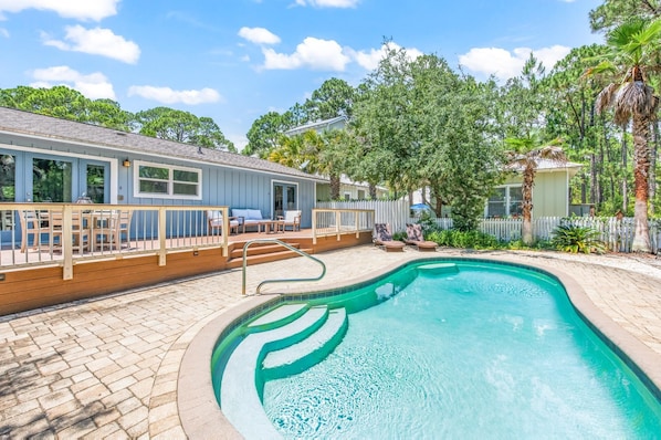 Relax by the pool surrounded by lush greenery and a house with a covered patio.