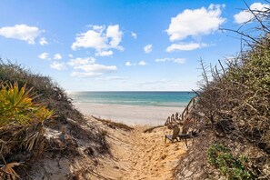 A sandy beach path leading to the ocean with a wooden bench and chair.