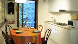 Comedor con mesa dispuesta para cuatro, cocina con armarios blancos, microondas y estufa a gas.