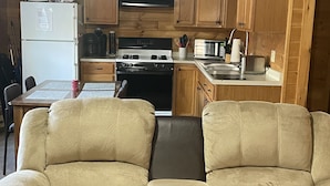 A compact kitchen with wooden cabinets, a refrigerator, stove, microwave, and a dining area with two leather sofas.