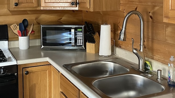 A kitchen with wooden cabinets, a microwave, a sink, and various kitchen utensils.