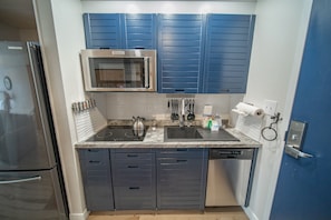 A modern kitchen with blue cabinets, stainless steel appliances, and a granite countertop. - Modern Studio with Balcony & Stunning Views! (Keystone)