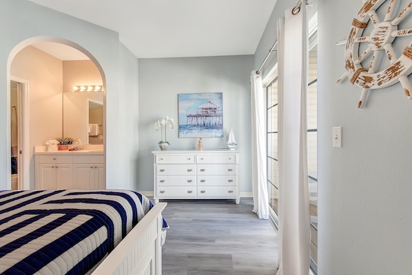 A bedroom with a bed, a dresser, a vanity, and a painting of a pier.