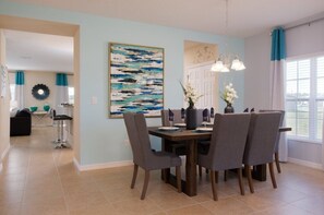 A dining area with a table set for four, chairs, a vase with flowers, and a painting on the wall. - Laurel Estates 278026 5 Bedroom Villa by RedAwning (Davenport)