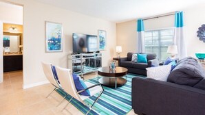 A modern living room with a sofa, armchair, TV, and a dining area with a table and chairs.