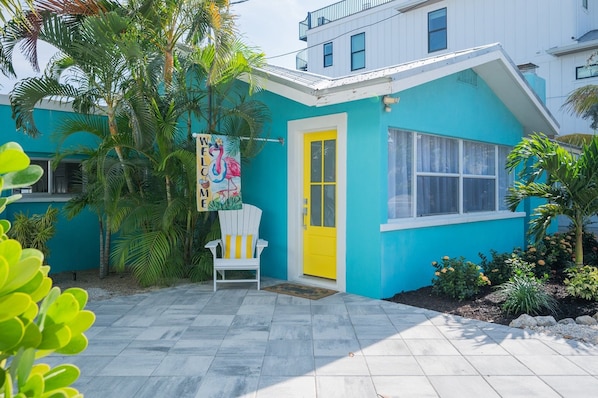 A turquoise house with a yellow door, a white chair, and a welcome sign.