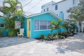 Une maison turquoise avec une porte blanche, une chaise blanche à l’extérieur et une pancarte sur laquelle on peut lire « BIENVENUE ».