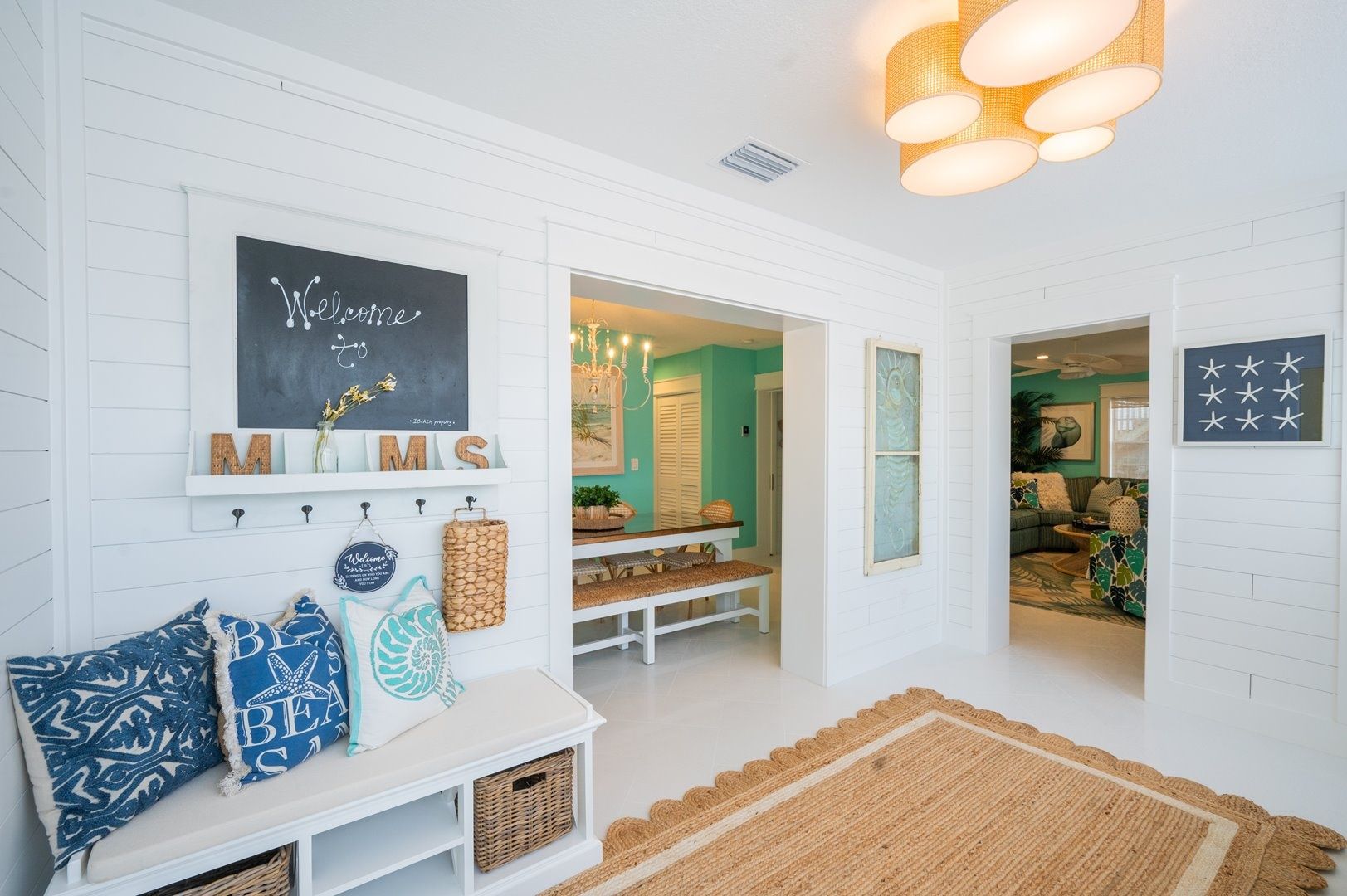 A room with a white wall, a chalkboard with 'Welcome' written on it, a bench with cushions, and a rug.