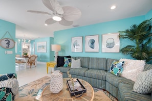A living room with a teal wall, a striped sofa, a round coffee table, and a ceiling fan.