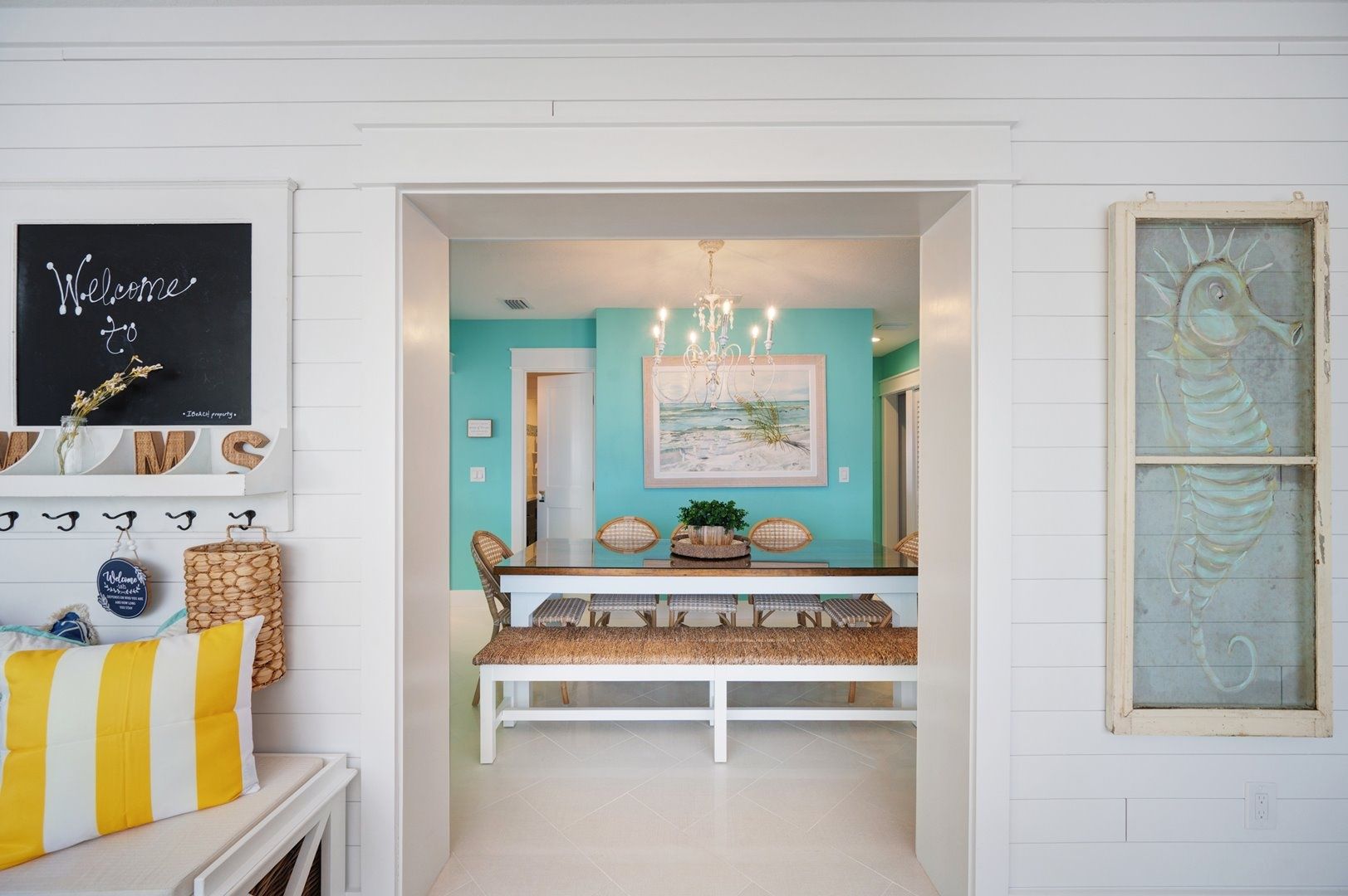 A hallway with a bench, a chandelier, and a framed seahorse artwork.