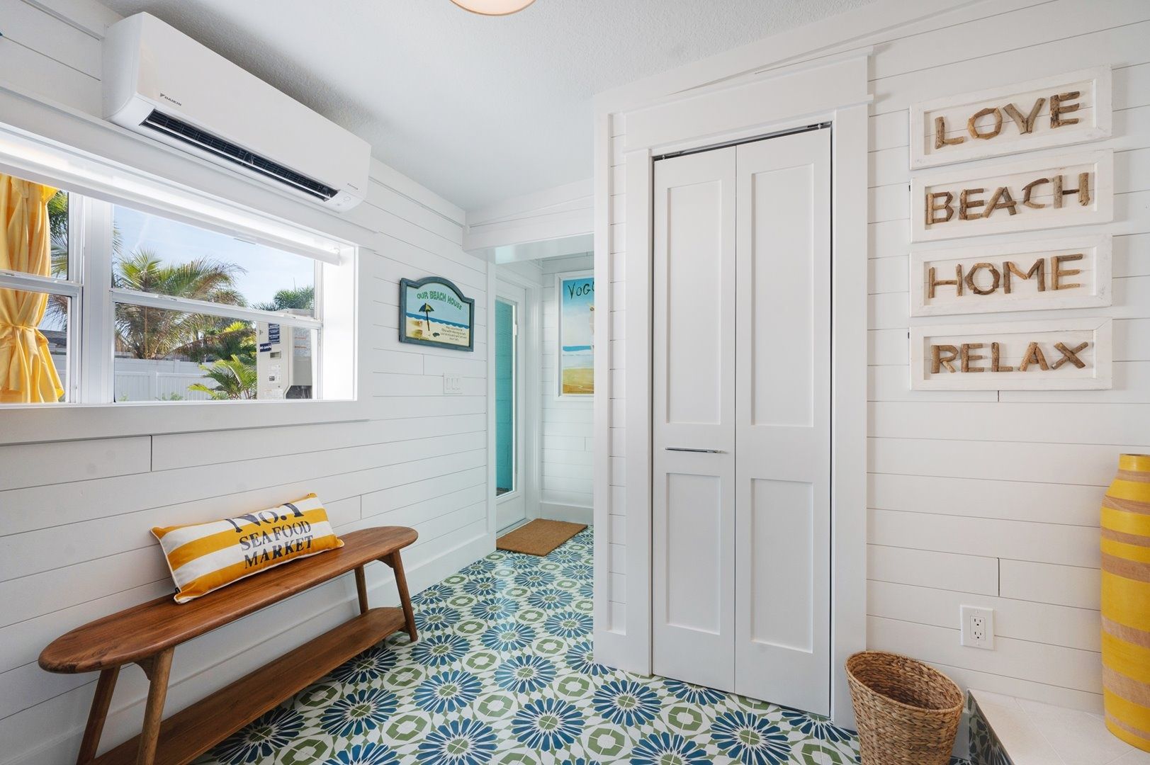A hallway with a bench, a door, and a wall with 'LOVE BEACH HOME RELAX' signs.