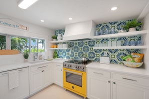 A modern kitchen with white cabinets, a yellow oven, and blue and green patterned backsplash tiles.