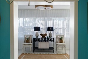 A room with a white sofa, a small table with two lamps, and a view through sheer curtains.