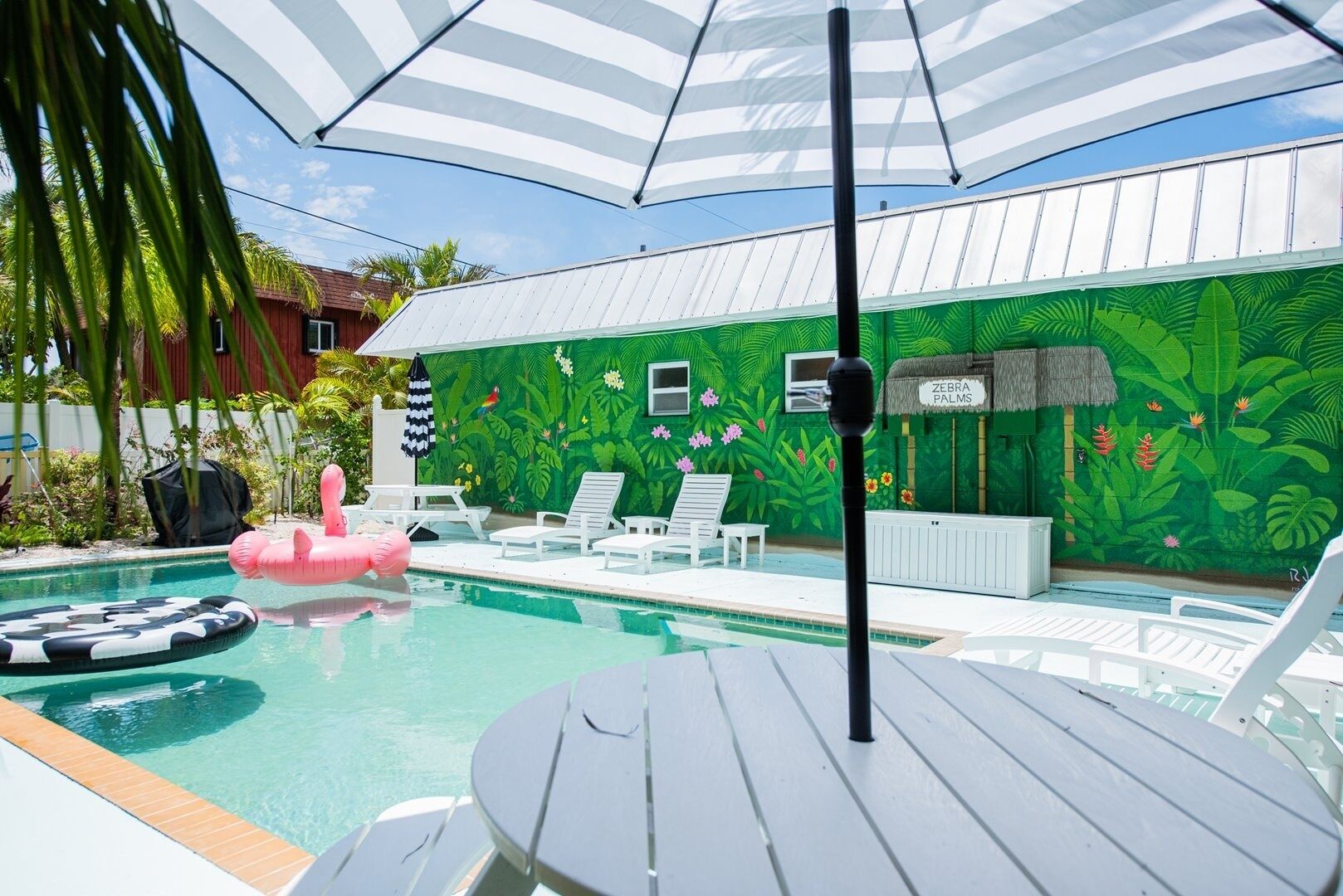 Zona de piscina amb un mural verd, cadiretes i una taula.