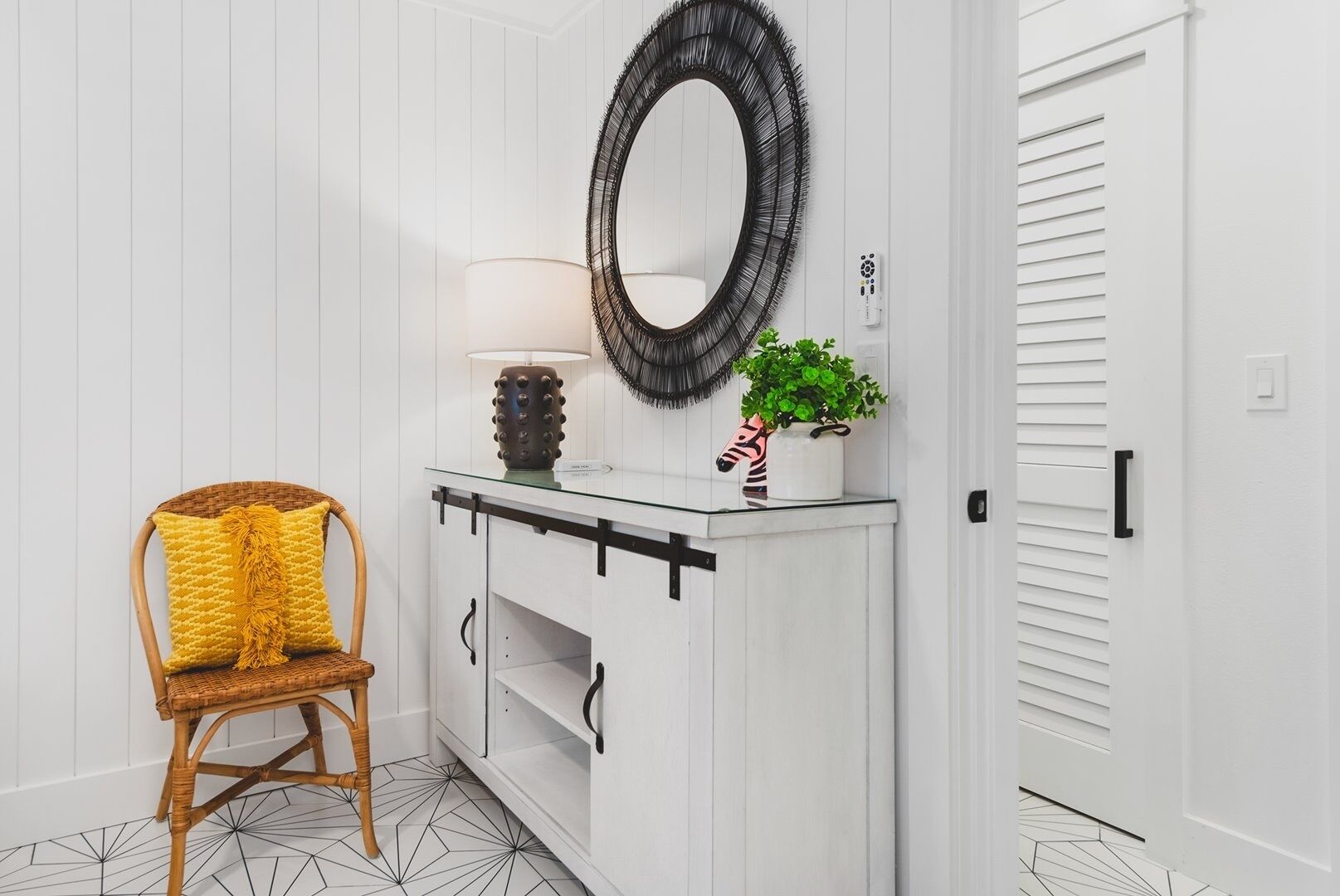 A white room with a wooden chair, a glass console table with a mirror, a lamp, and a zebra-patterned vase.
