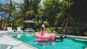 Uima-allas, jossa kelluu vaaleanpunainen flamingo, ja jonka ympärillä on palmuja sekä valkoisia aurinkotuoleja.