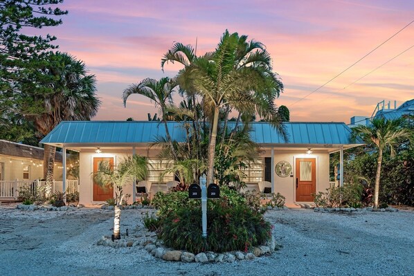 A two-story building with a blue metal roof, a covered porch, and a gravel driveway.