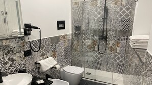 Une salle de bain moderne avec un mur recouvert de carreaux noirs et blancs formant un motif, un lavabo blanc, un bidet et une douche dotée d’une porte en verre.