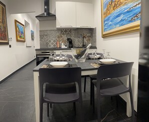 Une cuisine moderne avec une table à manger dressée pour deux personnes, comprenant des chaises noires, un saladier blanc et des verres à vin.